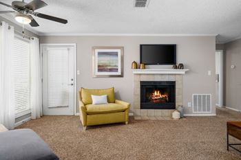 A carpeted living room which has a tile-surround fireplace, ceiling fan and a door to the patio.